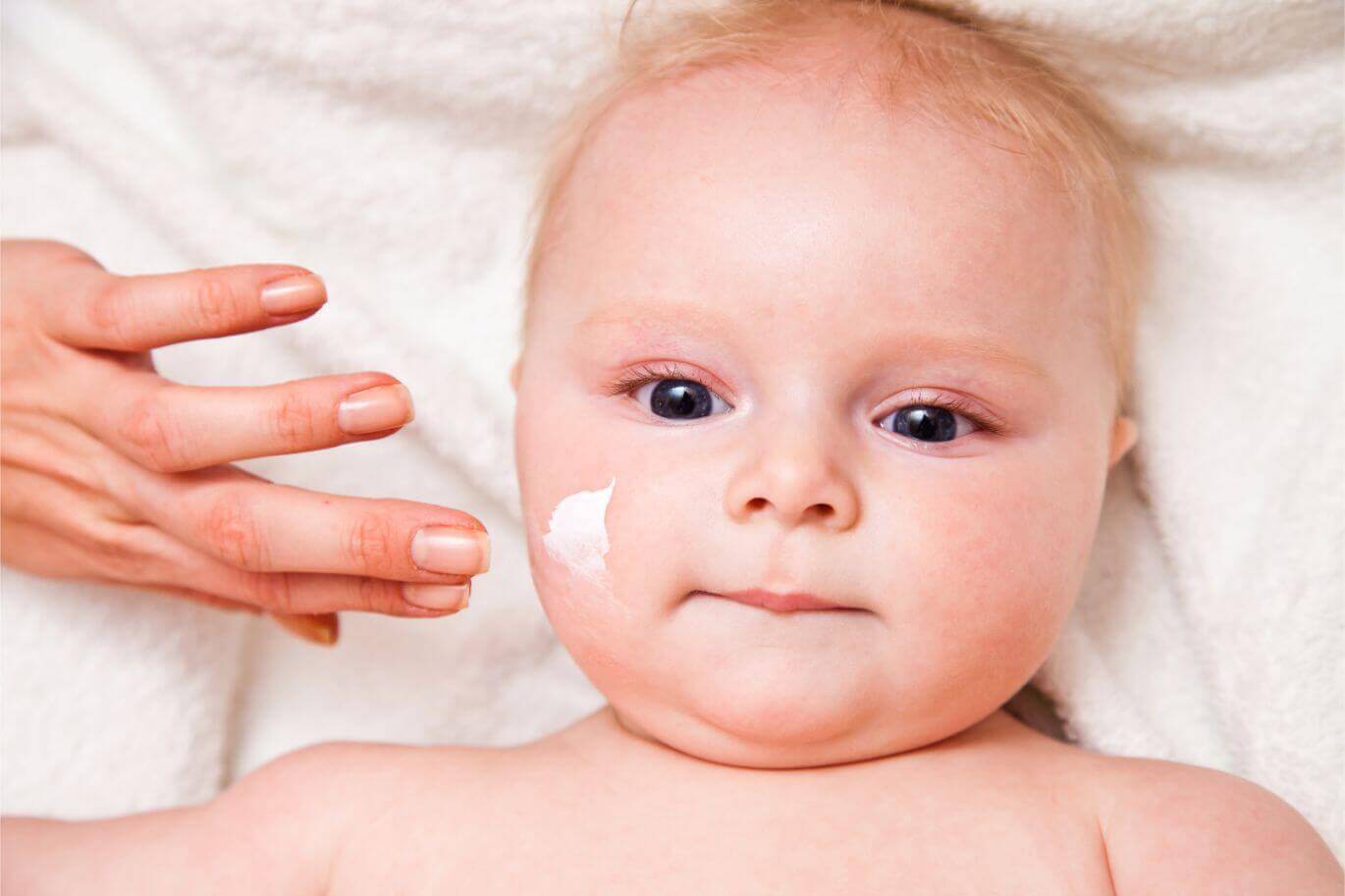 baby with skin care product on face with a white background